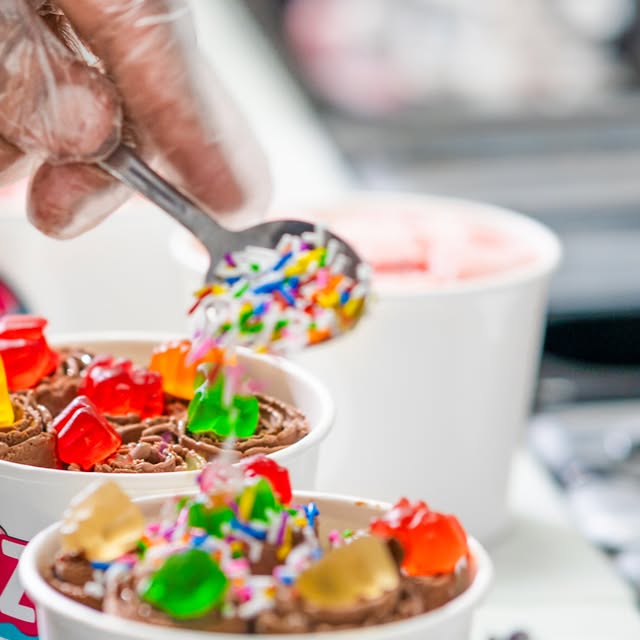 Chocolate ice cream rolls being topped with sprinkles and gummy bears